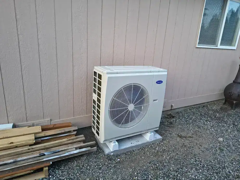 A new Carrier heat pump outdoor unit on its pad beside tan siding