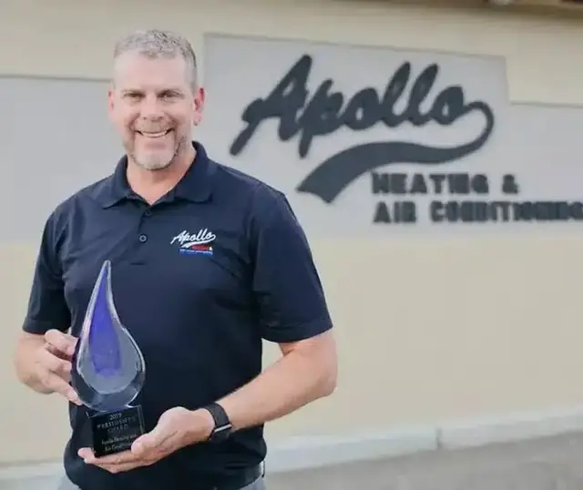 An Apollo team member holding a glass President's Award trophy in front of the Apollo sign