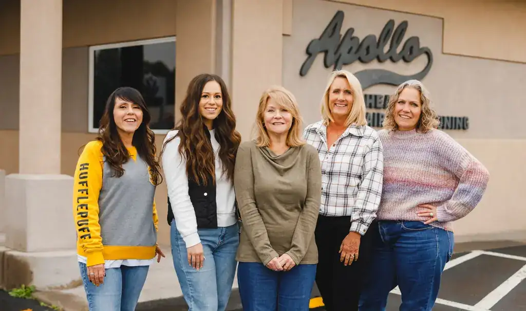 Five Apollo office staff standing at the building sign
