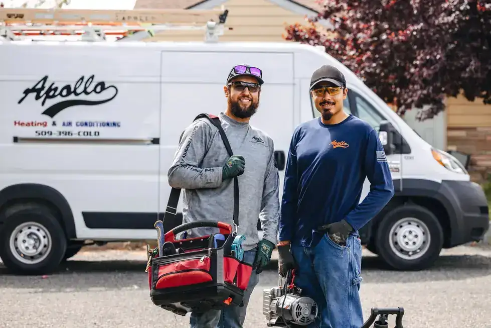 Two Apollo technicians with a tool bag and vacuum pump in front of a van lettered 509-396-COLD